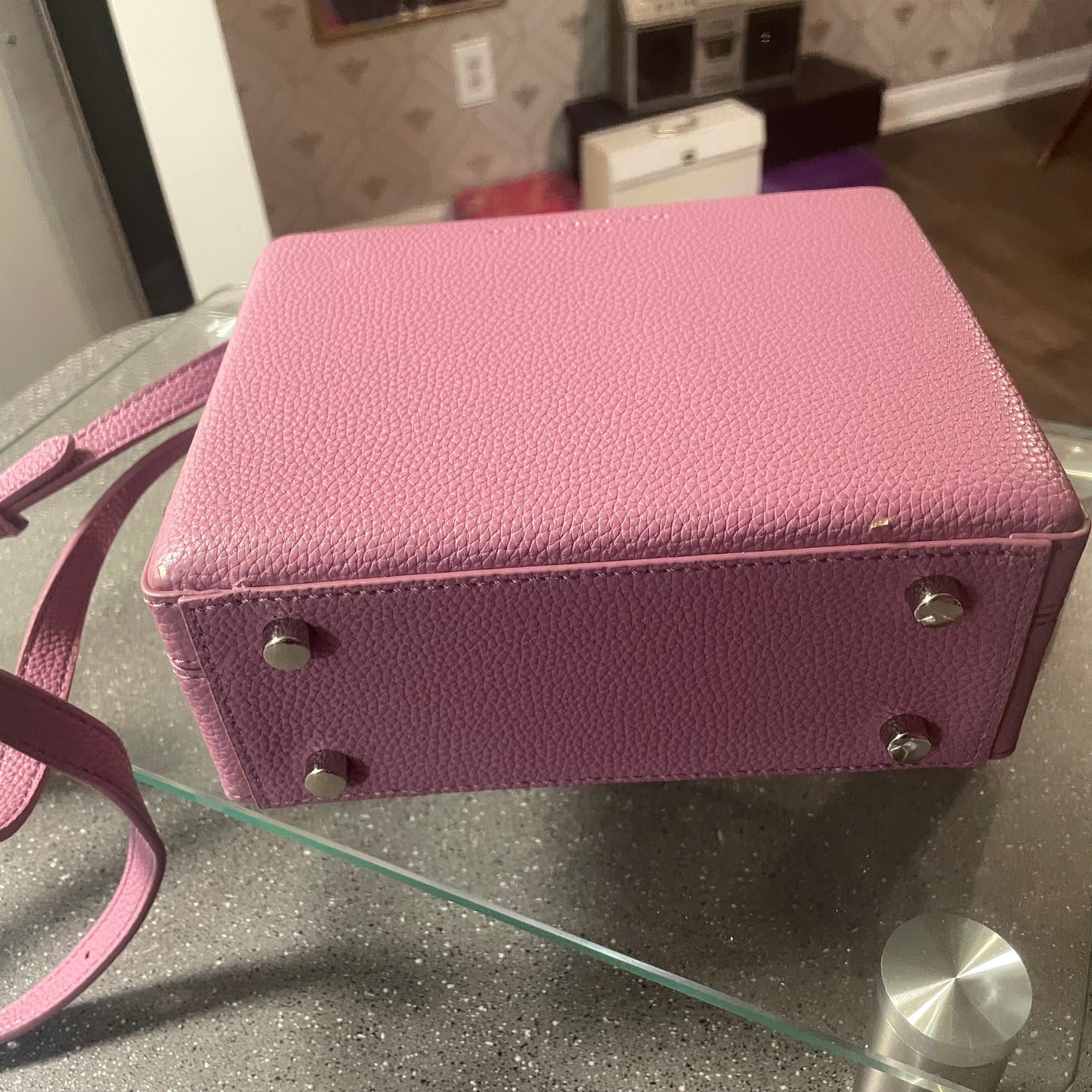 Pink textured handbag with a strap on a glass surface