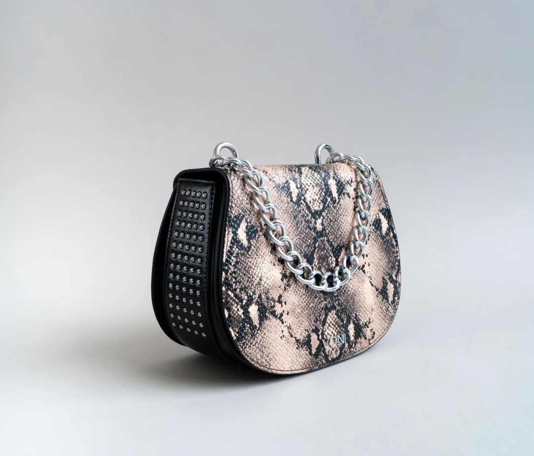 Designer handbag with chain detail and studded side on a light gray background